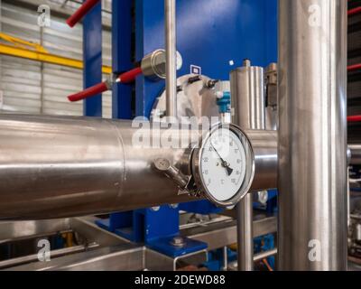 Industrial thermometer on a stainless steel pipe at an industrial workshop. Plate heat exchanger in the background Stock Photo