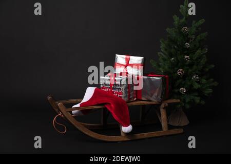 Rustic sleigh with gift boxes and Santas hat next to Christmas trees Stock Photo