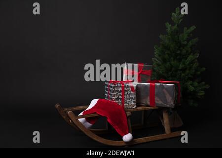 Rustic sleigh with gift boxes and Santas hat next to Christmas trees Stock Photo