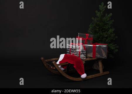 Rustic sleigh with gift boxes and Santas hat next to Christmas trees Stock Photo