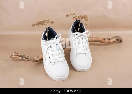 Ethical vegan shoes concept. A pair of white sneakers on the wooden snag, neutral beige craft paper background. Minimal style. Stock Photo