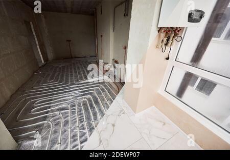 View from glazed loggia to new spacious room with warm floor. Electric floor heating. Pipe system of heating under white tiles, hidden gas boiler. Concept of home renovation and restoration. Stock Photo