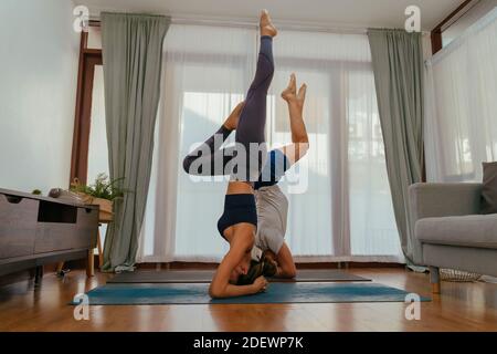 Side view of man and woman doing headstand on mats while practicing yoga in cozy living room at home Stock Photo