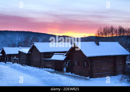 Irkutsk, Russia- 8 January 2019: Amazing winter landscape with traditional wooden houses and colorful sky during sunset in Ethnographic museum Taltci. Stock Photo