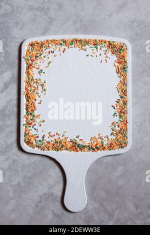 Wooden board with handle decorated with veins and colored noodles at the ends and space to input a text in the middle on a blue-gray marble background Stock Photo