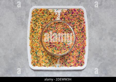 Overhead view of a round jar with colorful candies on a square white table with two divided parts of sugar noodles on a gray marble tile. Stock Photo