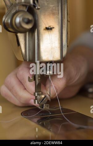 An old lady's hand with a needle threader on the sharp round point of an antique sewing machine. Stock Photo