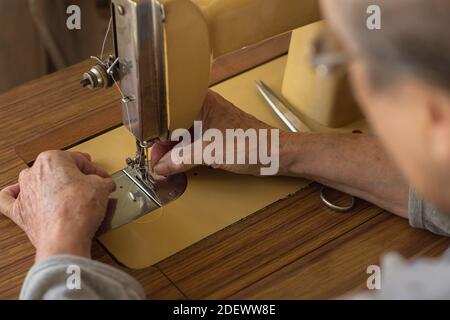 The hands of an elderly woman thread a needle into an old sewing machine on a wooden table. People at home. Stock Photo