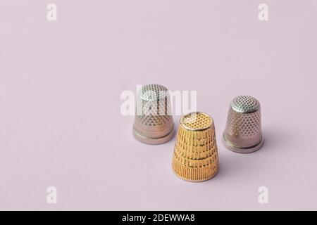 Triangular composition of three thimbles, two types, and one gold on a pink background. Sewing items. Stock Photo