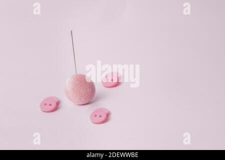 A textured cloth button rests on a long sewing needle surrounded by three pairs of small flat two-hole buttons. Buttons and pink background. Stock Photo