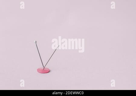 Two pearl head needles stuck in a two-hole button on a pink background. Stock Photo
