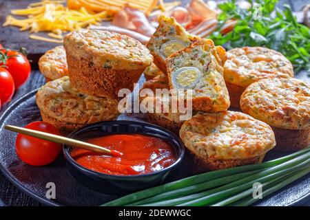 Bacon, Egg and Cheese Breakfast Muffins on a black plate on a wooden table  with ingredients, horizontal view from above Stock Photo
