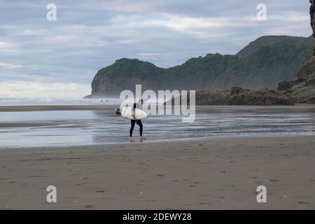 AUCKLAND, NEW ZEALAND - Feb 11, 2020: Auckland / New Zealand - February 11 2020: View of tired surfer walking on Piha beach Stock Photo