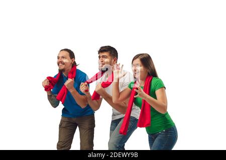 Hopeful. Three soccer fans woman and men cheering for favourite sport team with bright emotions isolated on white studio background. Looking excited, supporting. Concept of sport, fun, support. Stock Photo