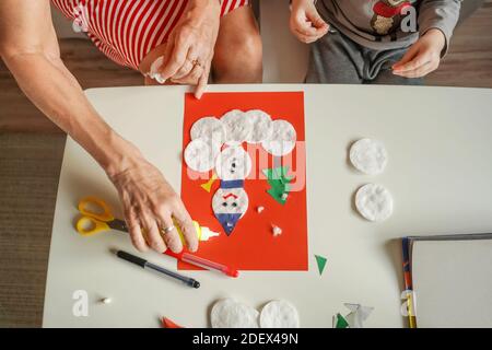 A Little boy with grandmother make Christmas craft, greeting card snowman. Top view. Stock Photo