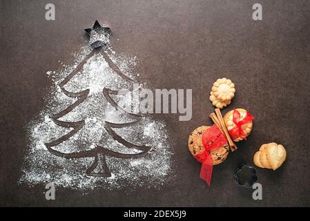 Christmas tree made from flour on a dark table, kitchen utensils and cookies. holiday, celebration and cooking concept. new year and christmas postcar Stock Photo
