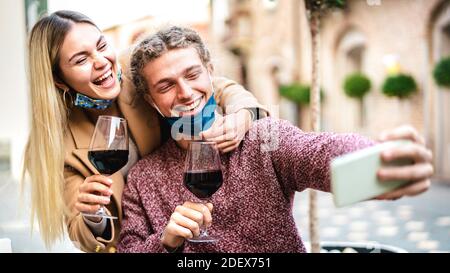Young couple in love with open face mask taking selfie at outside wine bar - Happy millennial lovers enjoying lunch together at restaurant patio Stock Photo