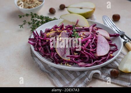 Red cabbage, pear and hazelnut salad with lemon and olive oil sauce. Light stone background. Vegetarian food. Selective focus. Stock Photo