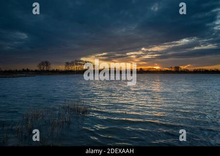 Sunset and dark clouds over the lake with reeds, spring evening view Stock Photo