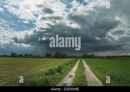 Empty dirt road through fields and a single cloud with rain, spring view, Nowiny, Poland Stock Photo