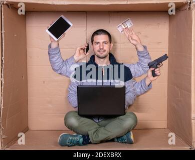 multi-tasking man sitting in a cramped cardboard office, working from home Stock Photo