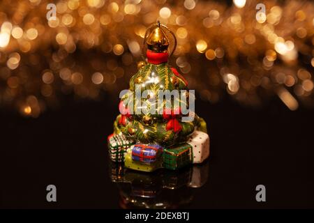 Christmas decoration. Glass Christmas tree decorated with red bows and surrounded by boxes with gifts on black glass with reflection. In the backgroun Stock Photo