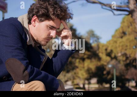 Close up young man aged 24-30 sitting in the street frustrated after being fired from his last job. Disgruntled man loses his office job. Stock Photo