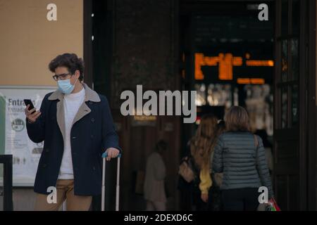 A recognizable young man with a mask on standing outside the train station with his suitcase calling a taxicab to pick him up. Business trip 2021. Stock Photo