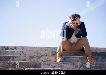 Panoramic young man aged 24-30 sitting in the street frustrated after being fired from his last job. Disgruntled man loses his office job. Stock Photo
