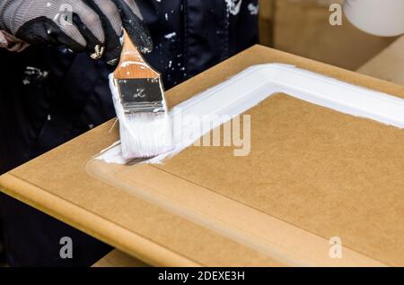 Repainting kitchen cabinet doors with white chalk paint indoors at home. Giving old kitchen new look concept. Hand holding a paint brush tool. Stock Photo