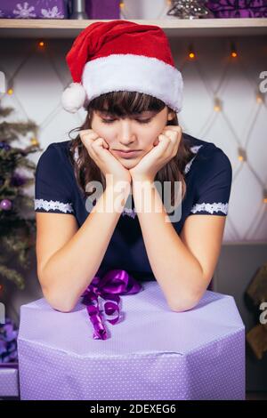 A teenage girl in a Santa hat is sad over a big Christmas present. Negative emotions Stock Photo