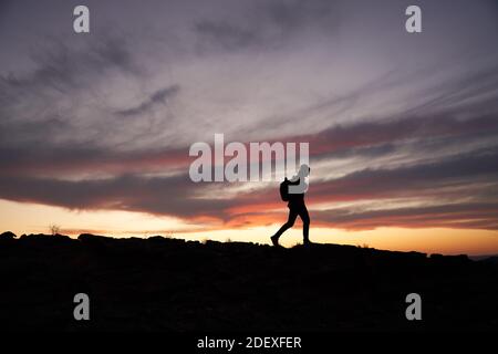 Silhouette of traveller with a backpack climbing up the mountain against beautiful horizon Stock Photo