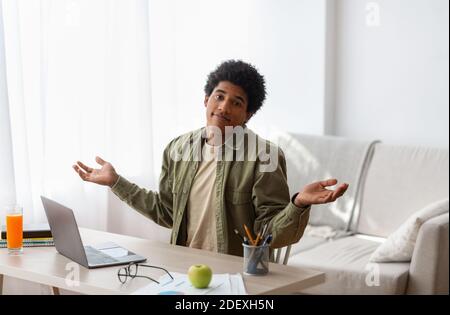 Puzzled black student sitting in front of laptop, not understanding difficult lesson, having difficulty studying online Stock Photo