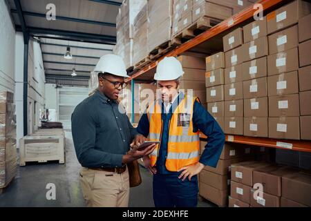 Male warehouse workers discussing about stock while using digital tablet Stock Photo