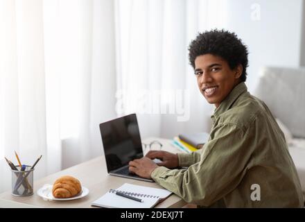Young happy teenage guy using laptop for remote studies at home, mockup for design on screen Stock Photo