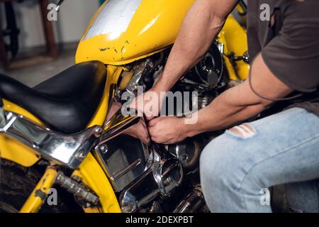 A strong male biker repairs his motorcycle in the garage. Interior of the workshop Stock Photo