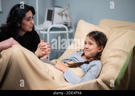A smiling cute girl in a hospital bed with her mother beside her. Stock Photo