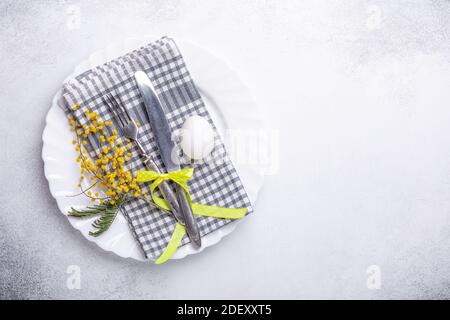 Easter table setting. White plate, mimosa flowers and cutlery on stone background. Top view Stock Photo