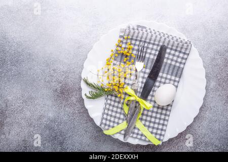Easter table setting. White plate, mimosa flowers and cutlery on stone background. Top view Stock Photo