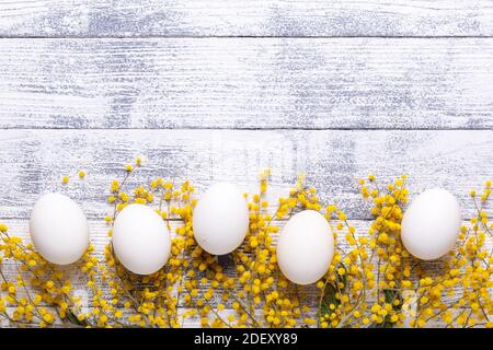 White eggs, mimosa flowers on a wooden table View from above Copy space Stock Photo
