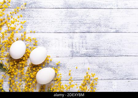 White eggs, mimosa flowers on a wooden table View from above Copy space Stock Photo