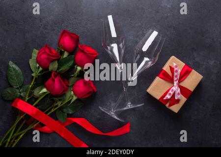 Red rose flowers bouquet, gift box, champagne glasses on black stone background Valentine's day greeting card Copy space Top view Stock Photo