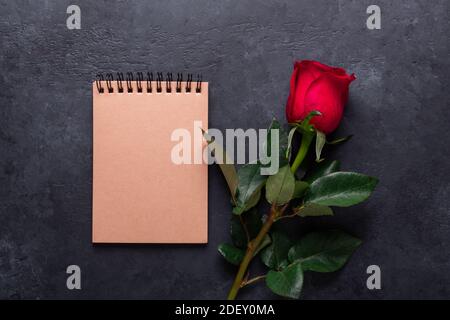 One red rose, notebook on black stone background Valentine's day greeting card Copy space Top view Stock Photo