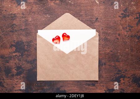 Craft envelope with red hearts on a vintage wooden background Piece of paper Valentine day concept Flat lay Top view Stock Photo