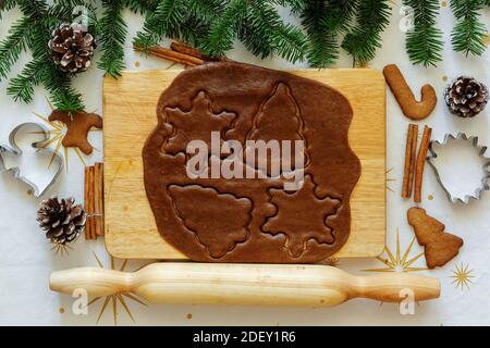 Gingerbread dough on a table with New Year's decor. Rolled out dough on the board. New Year's forms for cookies. New Year's layout. View from above Stock Photo