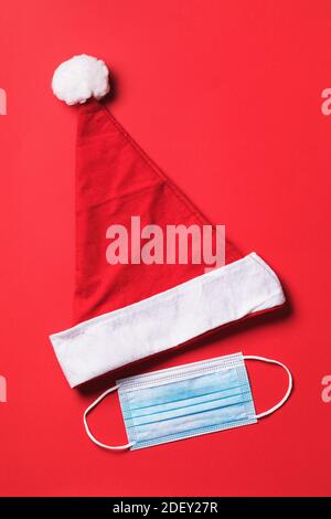 Santa Claus hat and medical mask on a red background, top view. Concept on the theme of quarantine during the Christmas holidays. Stock Photo
