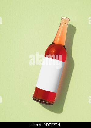 One full transparent glass beer bottle laying on light green surface. Bottle with blank white label and red liquid inside, shadow on background. Retro Stock Photo