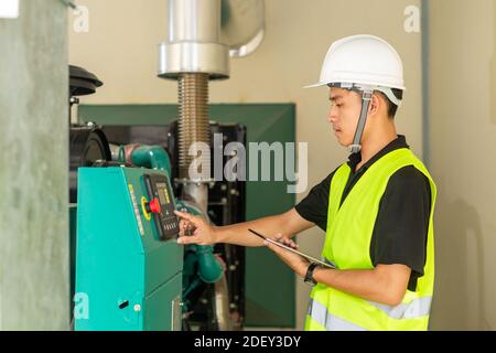 Asian maintenance technician checking technical data of water pressure control system equipment in factory. Stock Photo