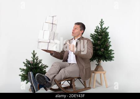 Christmas themed horizontal business portrait of a smart casual dressed male executive sitting on a sleigh juggling white wrapped gift boxes all set o Stock Photo