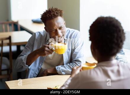 Attractive black guy with his girlfriend drinking coffee and having pleasant conversation at urban cafe Stock Photo